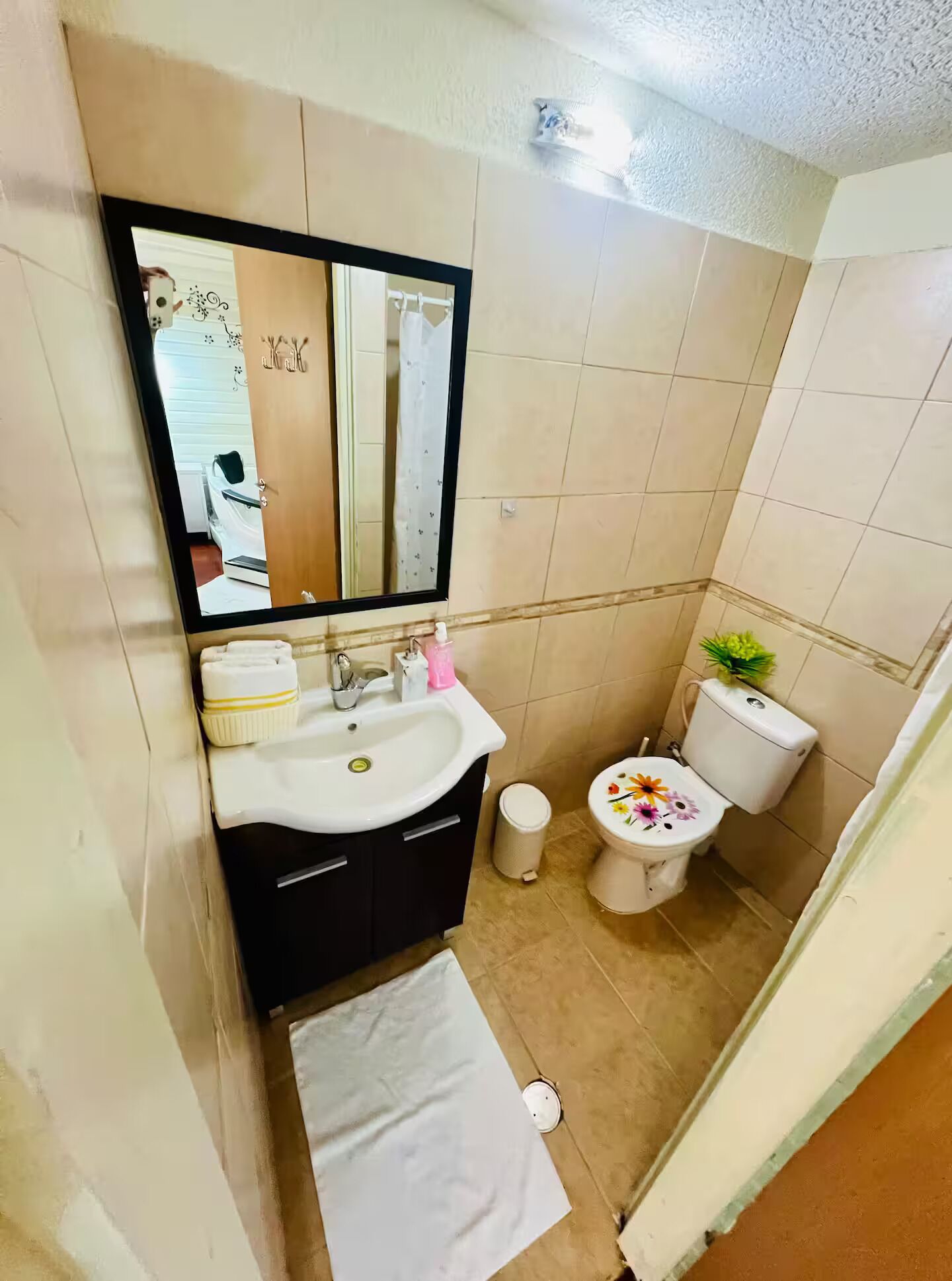 A bathroom with a sink, mirror, toilet, and a small trash bin.