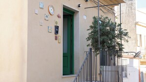A building facade with a green door, a small tree, and various decorative tiles. - Lues Rooms (Ragusa)