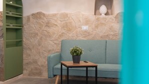 A room with a stone wall, a green sofa, a wooden table with a potted plant, and a green shelving unit. - Lues Rooms (Ragusa)