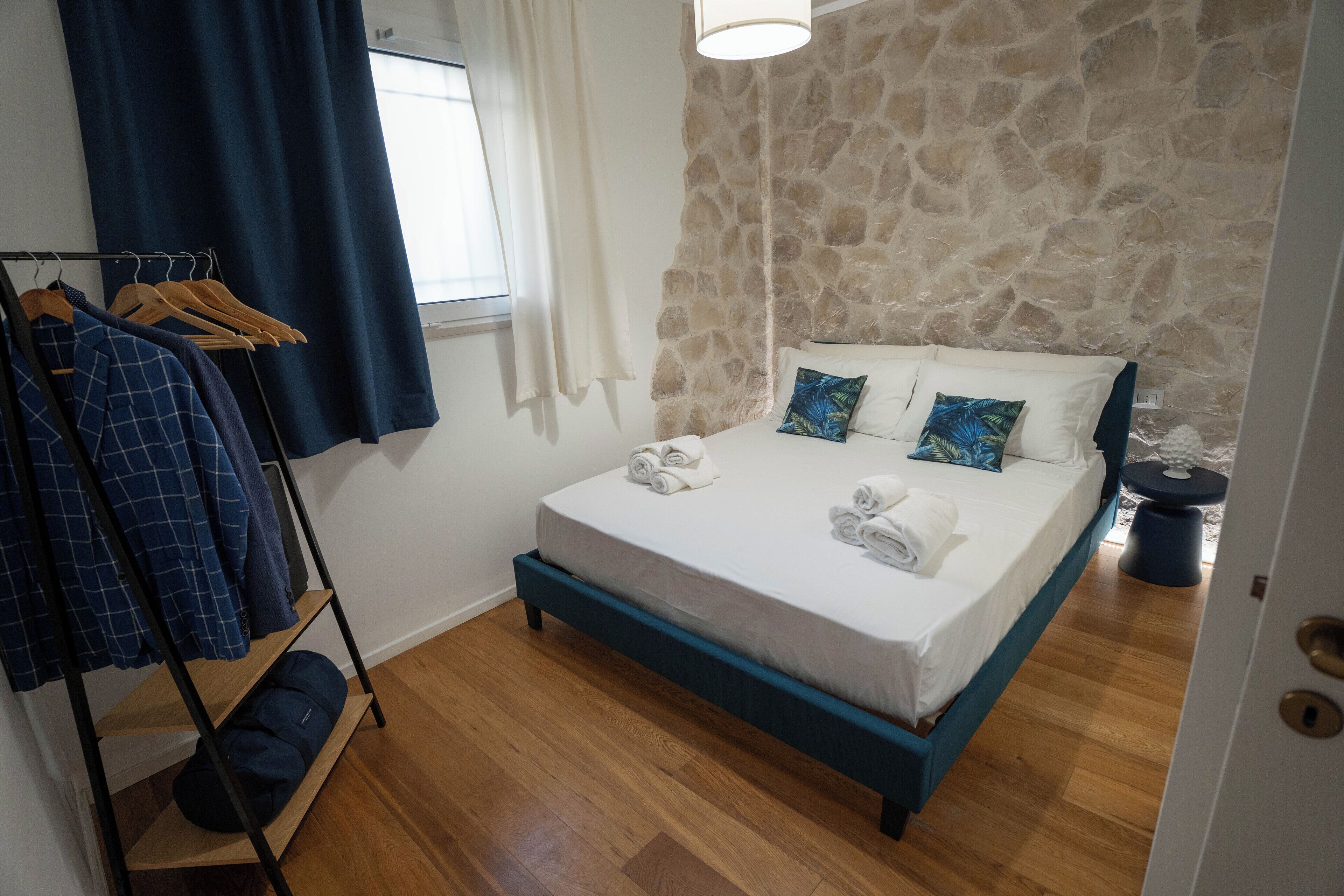 Un dormitorio con pared de piedra, cama con ropa blanca y suelo de madera.