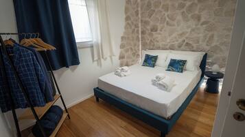 Un dormitorio con pared de piedra, cama con ropa blanca y suelo de madera.
