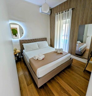 Una habitación de hotel con cama, espejo redondo, mesita de noche con lámpara y ventana con cortinas.