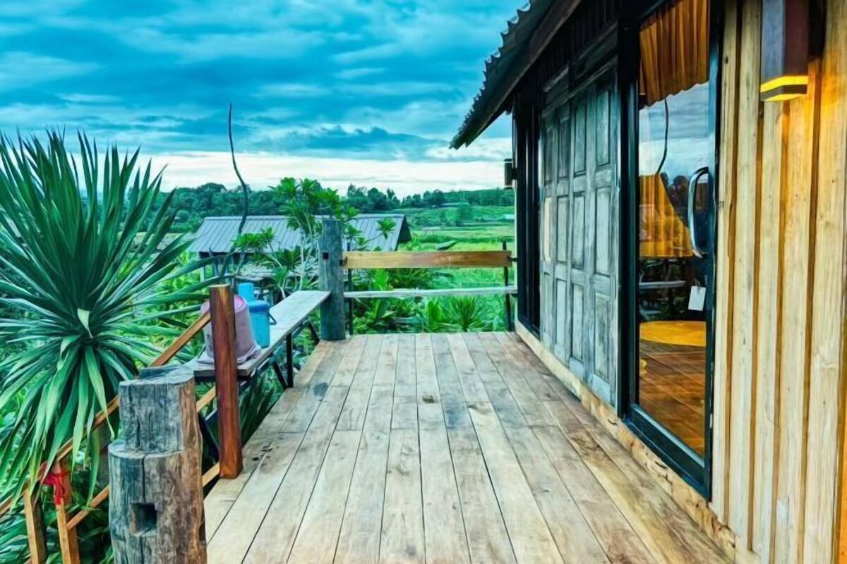 A wooden deck with a view of a green landscape, a wooden fence, and a building with large windows.