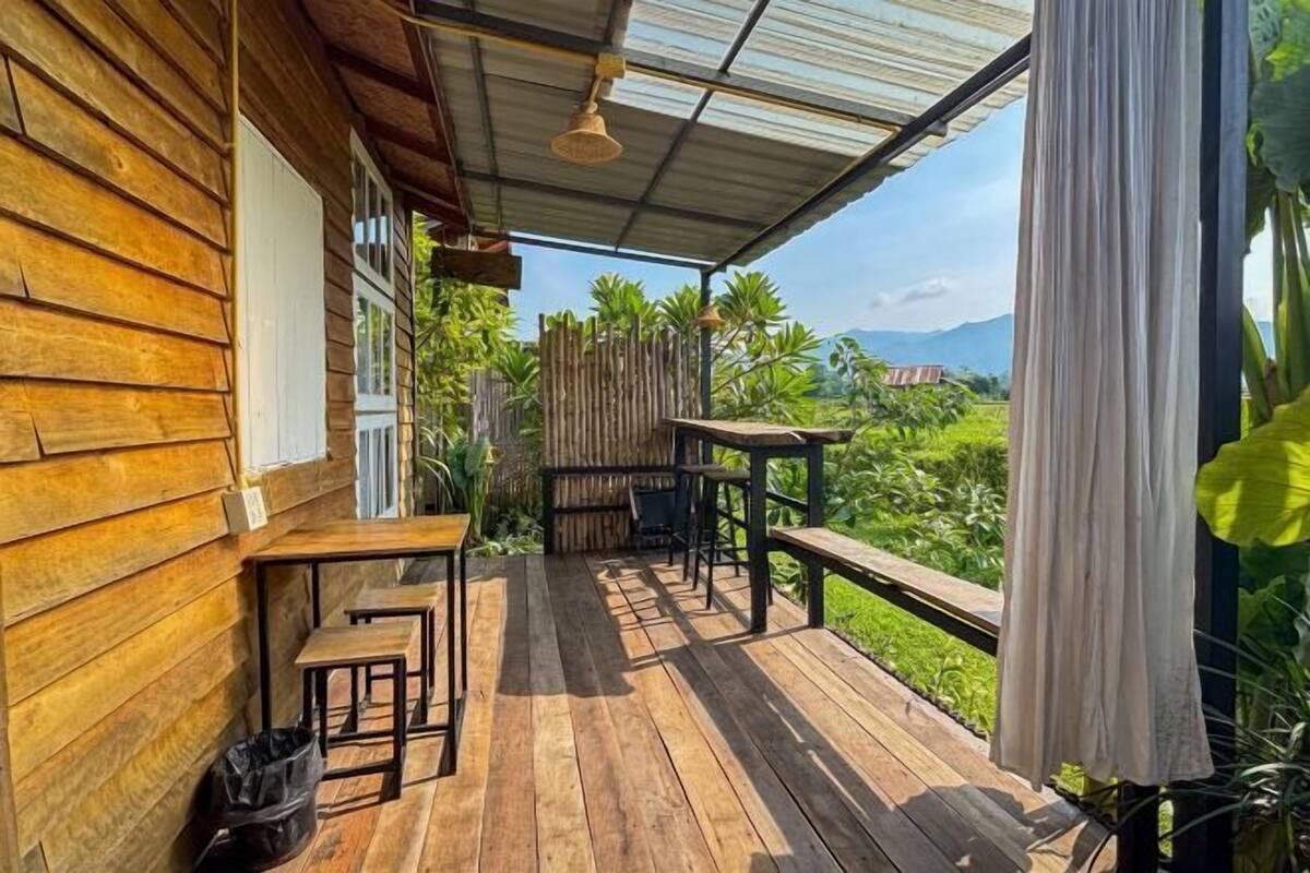 A wooden deck with outdoor seating, a covered area with a metal roof, and a view of greenery and mountains in the background.