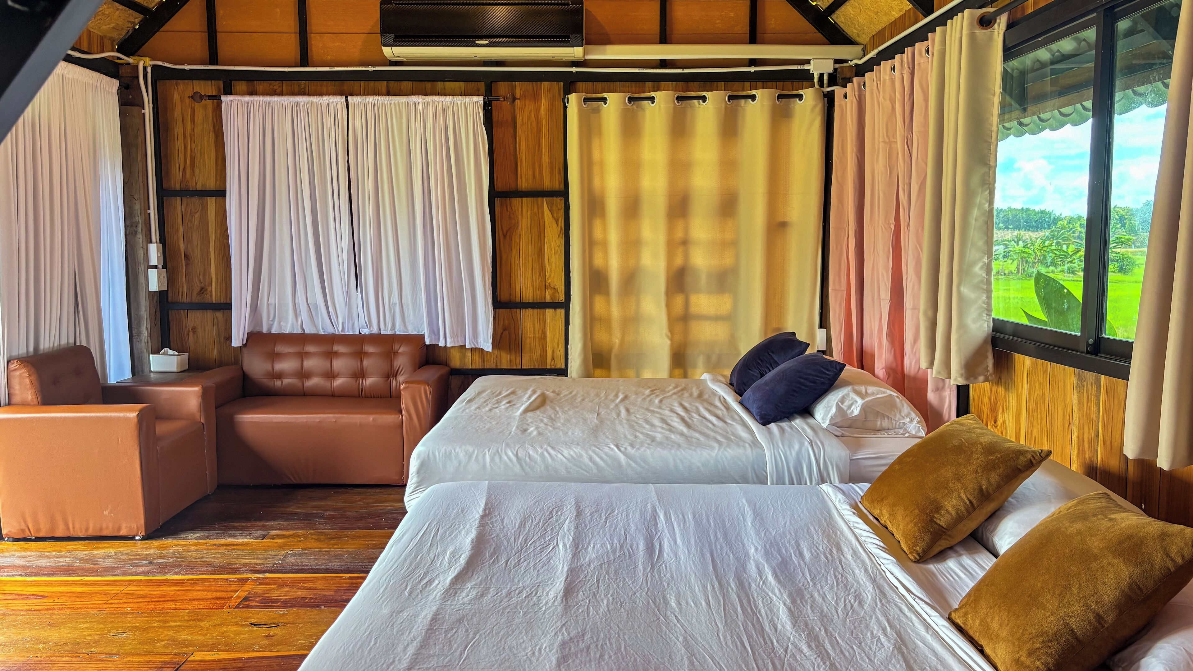 Un dormitorio con cama, dos almohadas, una mesita de noche, una silla y cortinas.