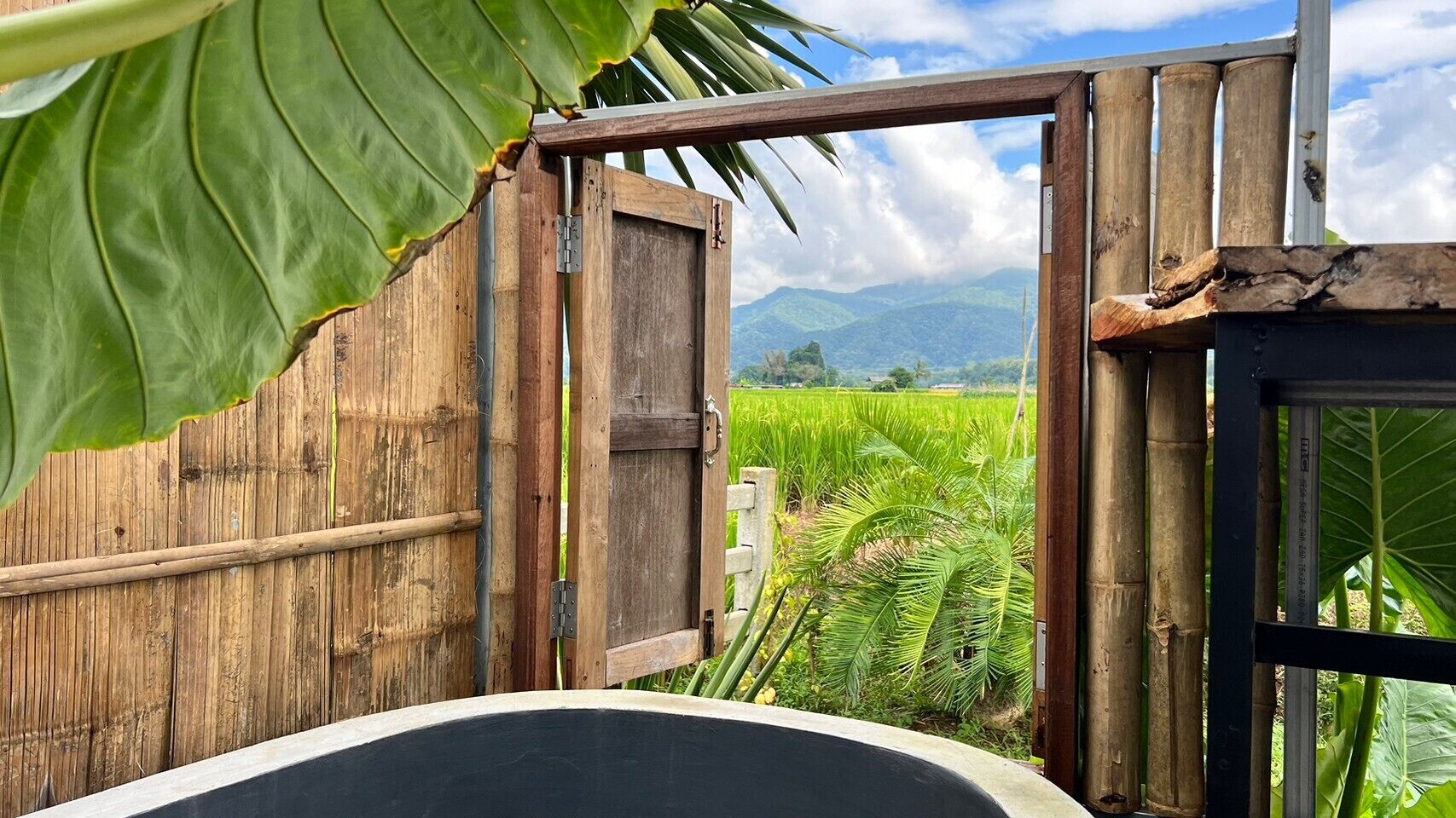 Una puerta de madera rústica que da a un campo verde exuberante con montañas al fondo.