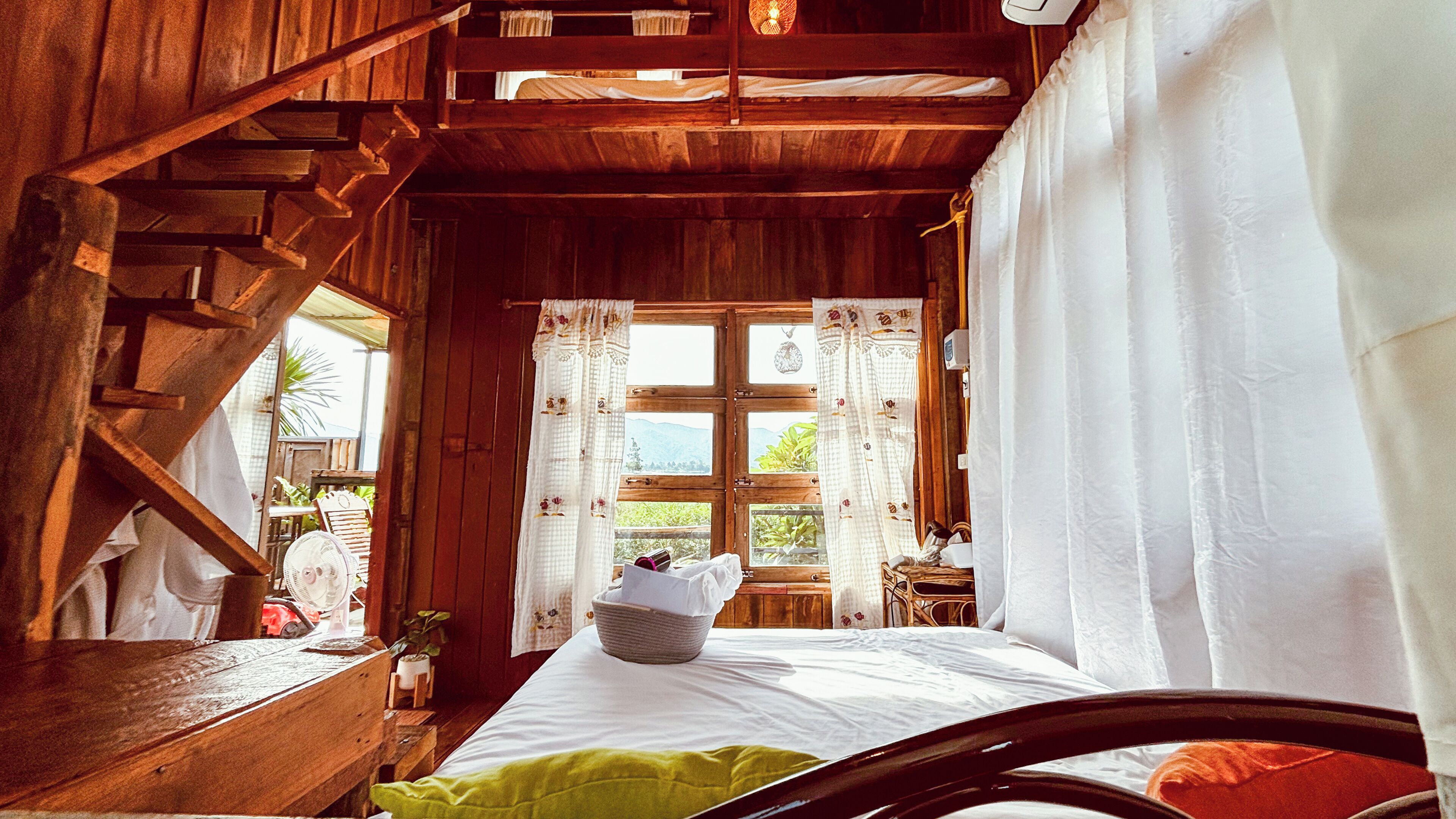 A rustic wooden room with a bed, a small table, and a window with curtains.