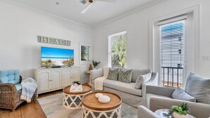 A spacious living room with a sofa, two round wooden coffee tables, a wicker chair, and a television on a cabinet. - 🌞The Rooftop on 30A | Stunning Rooftop Gulf Views | Easy Beach Access🌞 (Santa Rosa Beach)