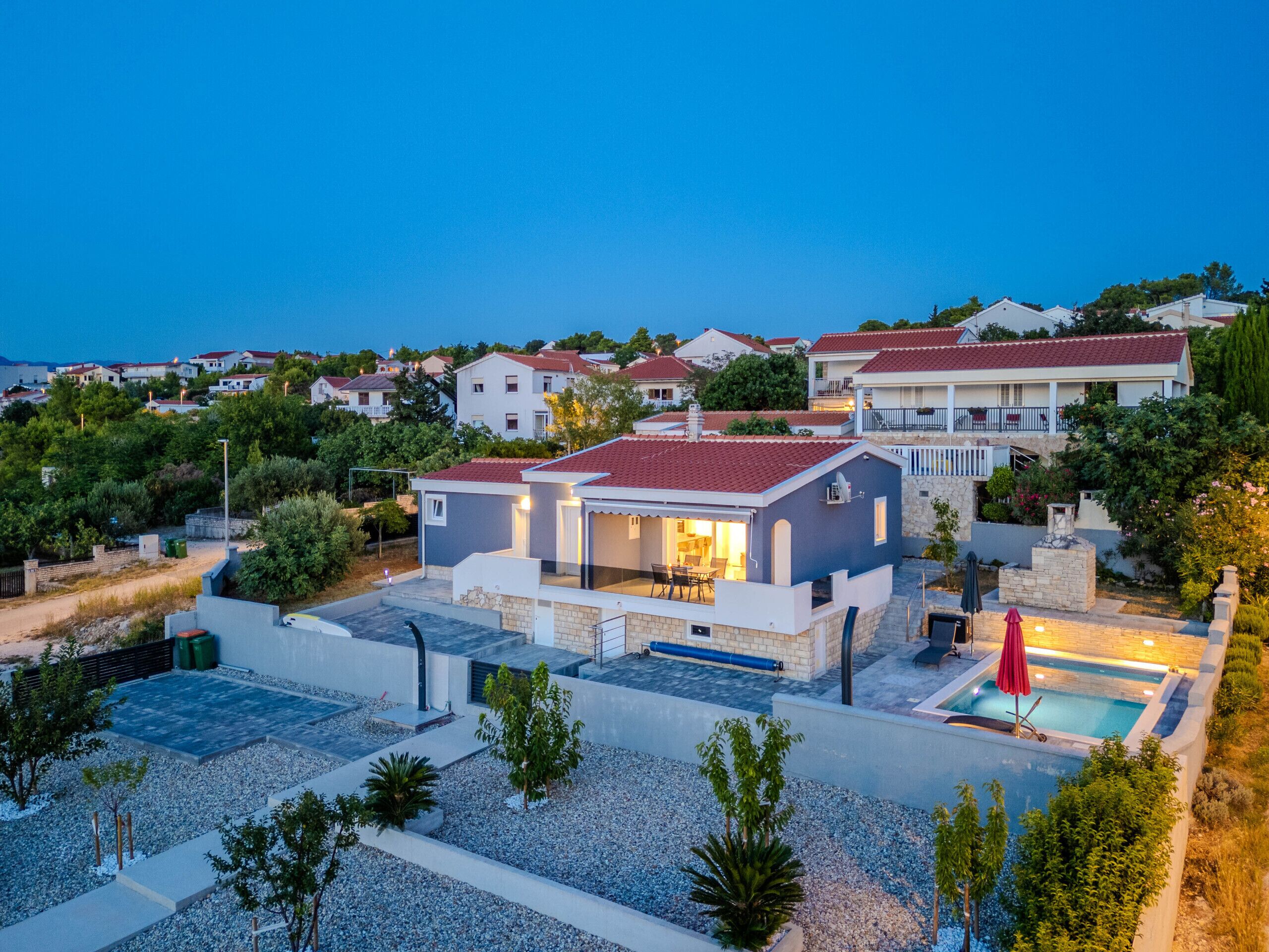 Une villa moderne dotée d’une piscine, entourée d’une végétation luxuriante et d’autres immeubles résidentiels.