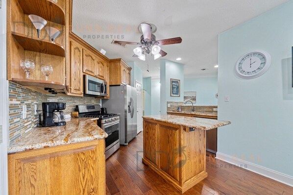 A kitchen with wooden cabinets, a granite countertop, a built-in oven, a refrigerator, and a ceiling fan.