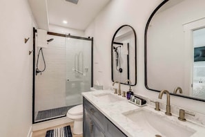 A modern bathroom with a glass shower enclosure, a double sink vanity, and a large mirror.