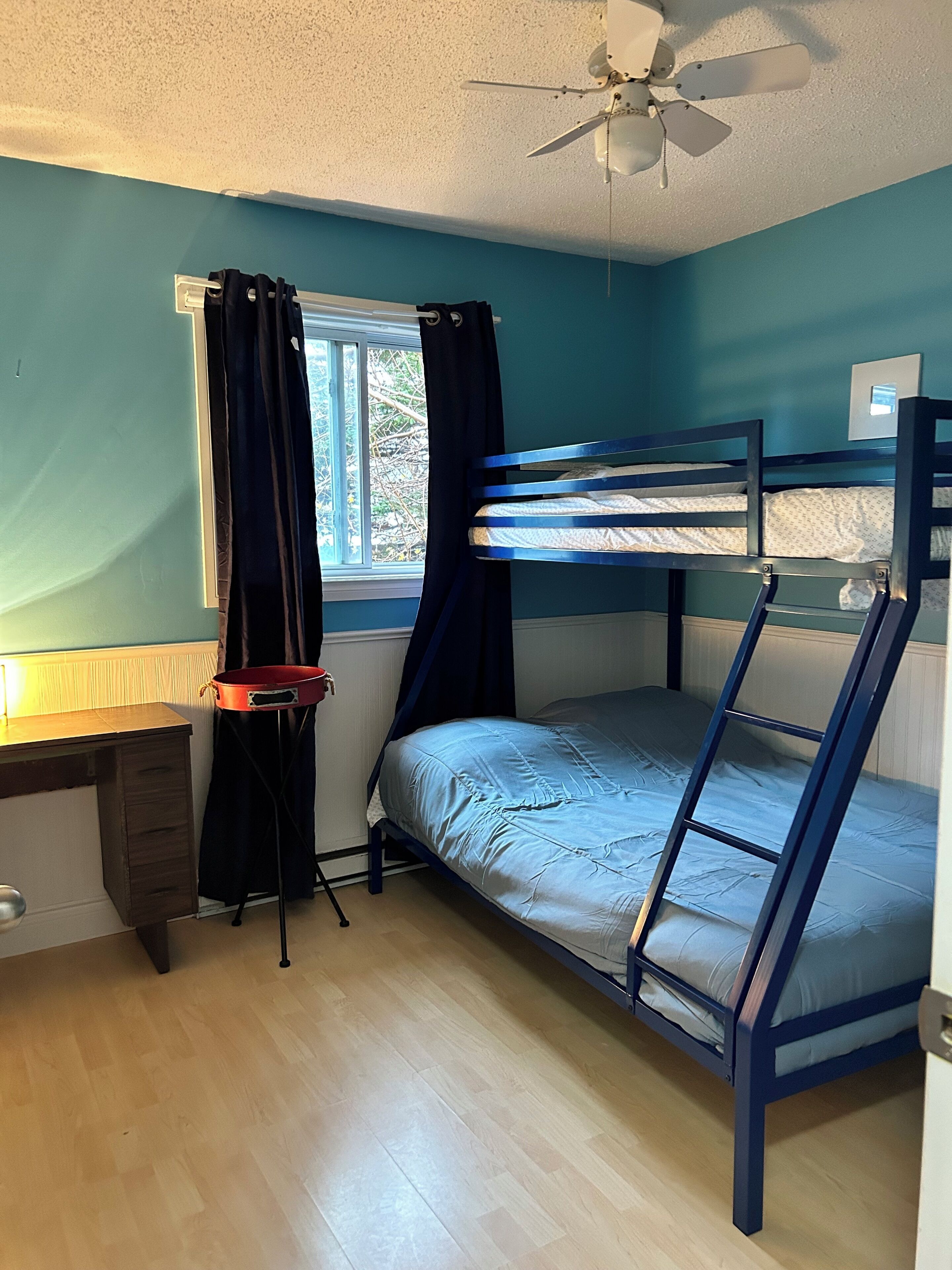A bunk bed room with a desk and a window.