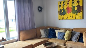 Un salon avec un canapé d’angle, une table basse et une grande fenêtre avec des rideaux.