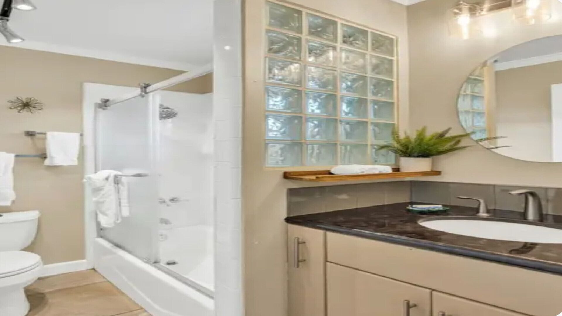 A modern bathroom with a glass shower enclosure, a white toilet, a bathtub, a vanity with a sink, and a mirror.