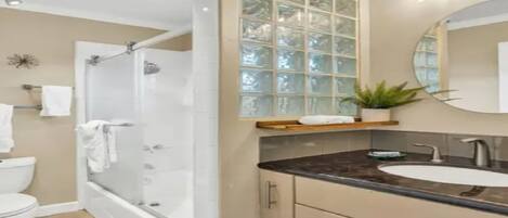 A modern bathroom with a glass shower enclosure, a white toilet, a bathtub, a vanity with a sink, and a mirror.