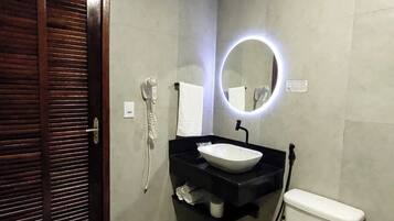Un baño con puerta de madera, inodoro blanco, lavabo negro y espejo encima, además de un perchero para toallas.