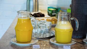 Um buffet de café da manhã com dois jarras de sucos de frutas, identificadas como 'Suco de Laranja' e 'Suco de Maracujá', em uma bancada de mármore.