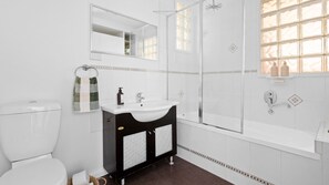 Bathroom features a toilet, sink, and glass-enclosed shower area with a large mirror above the sink and a window.