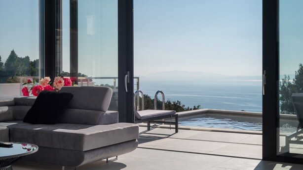 Un espace extérieur moderne aménagé avec un coin salon, une piscine, un canapé et une table, offrant une vue panoramique sur la mer et les montagnes.
