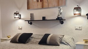A bedroom with a bed, pillows, a nightstand, a wall-mounted shelf with decorative items, and a painting. - APARTMENT FOR RENT IN TORREVIEJA 1st FLOOR IN SPAIN opposite tennis club (Torrevieja)