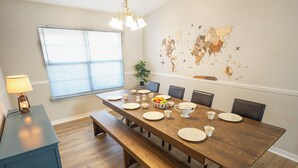Un espace repas avec une grande table en bois, des bancs et une carte du monde accrochée au mur.