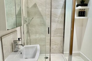Une salle de bain moderne avec une douche à parois de verre, un lavabo blanc et une étagère contenant des articles de toilette.