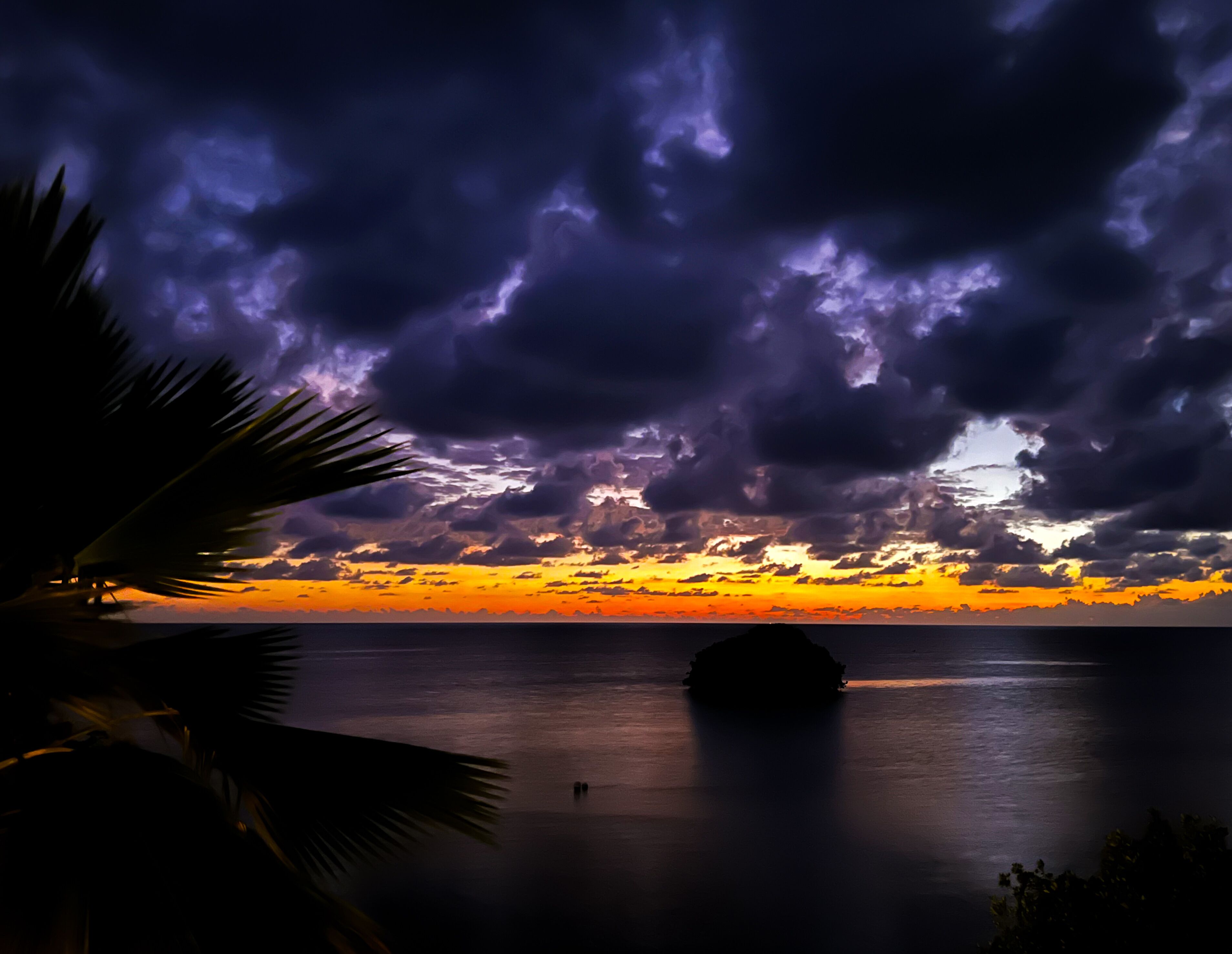 A sunset over a calm sea with a silhouette of a small island.