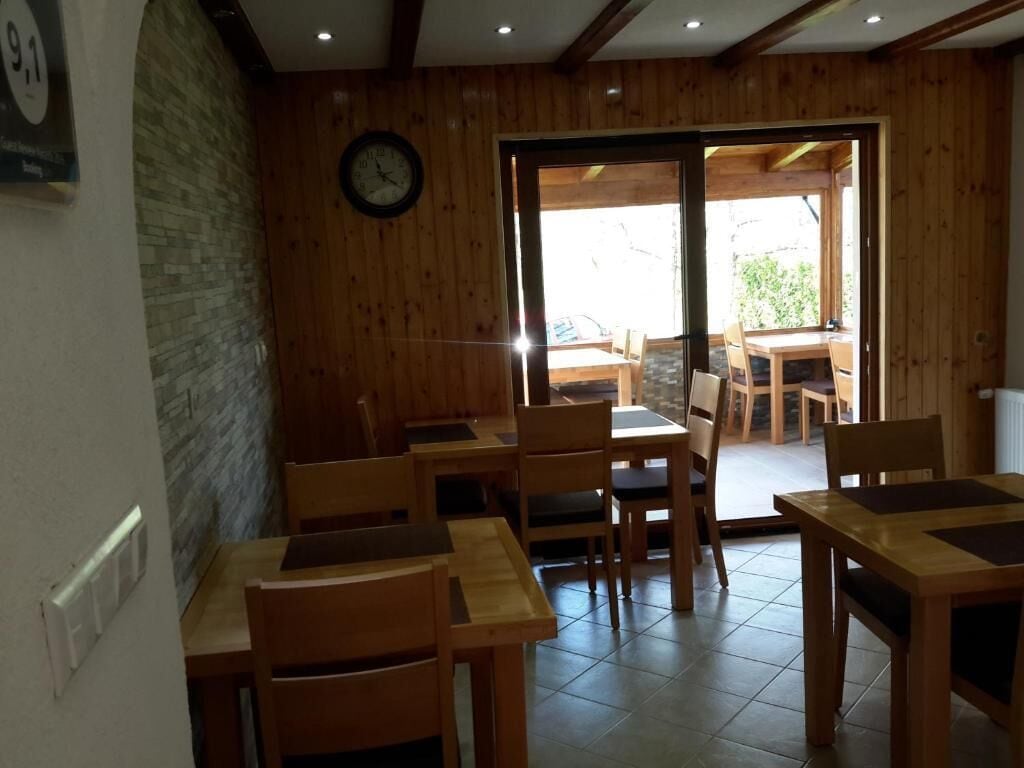 Interior de madera con mesas y sillas, un reloj en la pared y una puerta que da al exterior.