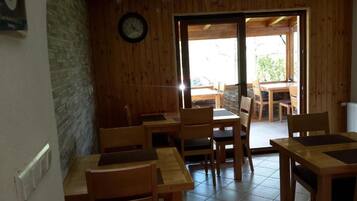 Interior de madera con mesas y sillas, un reloj en la pared y una puerta que da al exterior.
