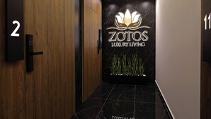 A modern hallway with a black marble floor, a wooden door labeled '2', and a wall with the 'ZOTOS LUXURY LIVING' logo.