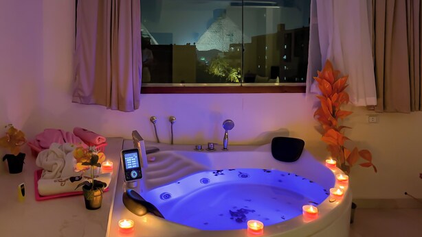 A modern bathroom with a bathtub, a digital control panel, and multiple candles. - Panorama Pyramids Jacuzzi (Giza)