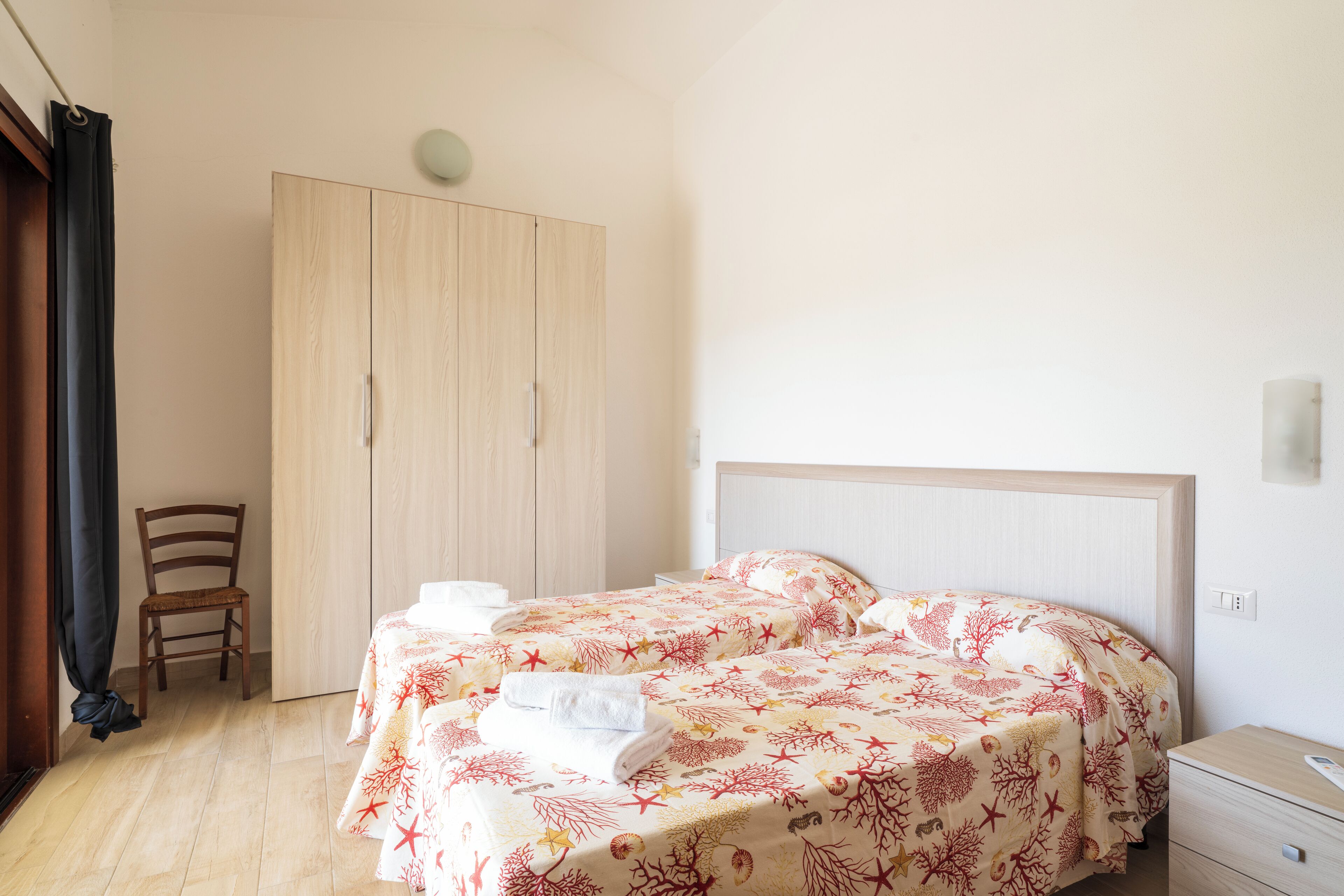 Ein Schlafzimmer mit zwei Betten, einem Holzschrank, einem Sessel und einem Nachttisch.