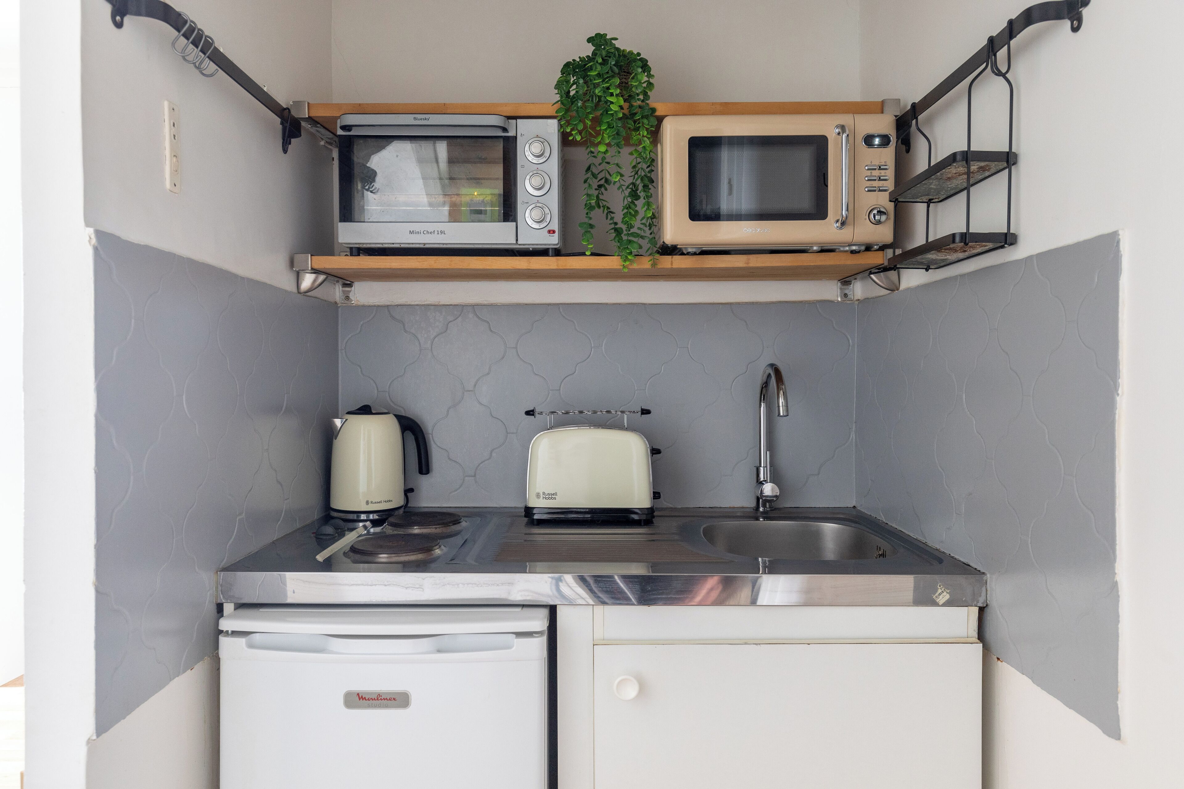 A compact kitchen with a built-in microwave, toaster, kettle, and a small refrigerator.