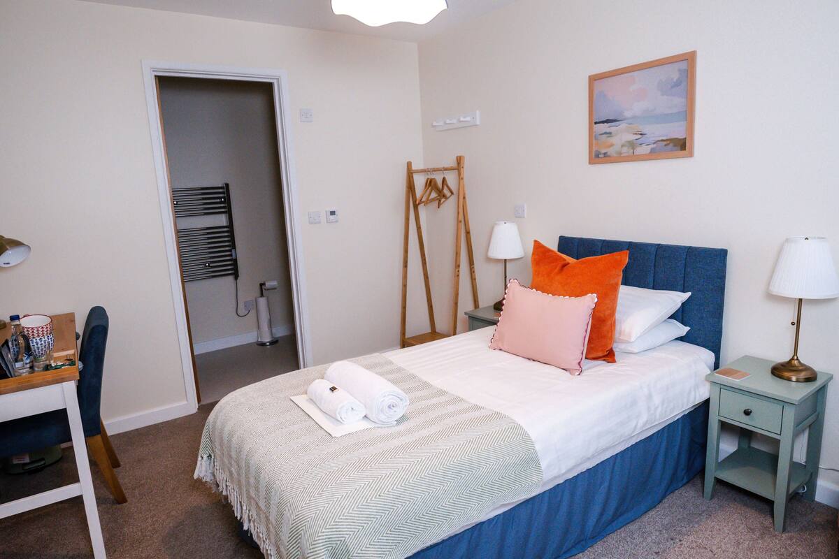 A neatly arranged bedroom with a bed, bedside tables, a desk, and a chair.