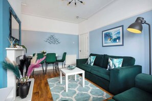 A living room with a green sofa, a white coffee table, and a painting on the wall.