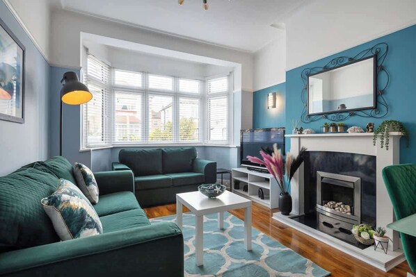 A living room with a green sofa, a white coffee table, a fireplace, and a bay window.