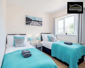 Une chambre d’hôtel avec deux lits, une fenêtre avec des rideaux, un tableau au mur et un logo dans le coin supérieur droit.