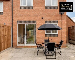 A brick house with a patio, a sliding glass door, and a table with chairs.