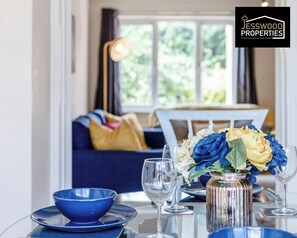 Un coin repas avec une table dressée pour deux personnes, un vase rempli de fleurs et un canapé en arrière-plan.