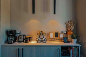 A kitchenette with a coffee maker, kettle, mug, and a two-tiered coffee station.