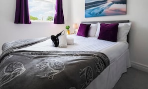 Ein ordentlich bezogenes Bett mit einem gemusterten  Überwurf, eine kleine Pflanze auf dem Nachttisch und ein Bild über dem Bett.