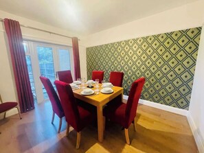 A dining area with a table set for four, red chairs, and a patterned wall. - Contractor Friendly | 2 Bath |Free Parking | Wifi (Central Bedfordshire)