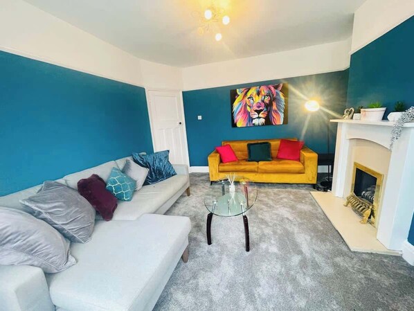 A living room with a white sofa, a glass coffee table, a yellow sofa, and a fireplace. - Contractor Friendly | 2 Bath |Free Parking | Wifi (Central Bedfordshire)