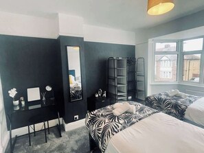 A bedroom with two beds, a desk, a mirror, and a wardrobe.
