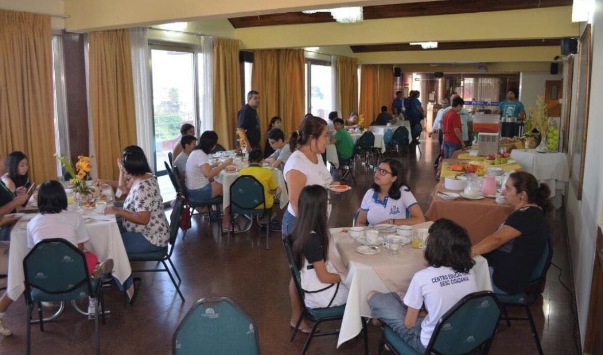 Un espace repas avec des tables et des chaises, des personnes qui déjeunent ou dînent, et un buffet en arrière-plan.