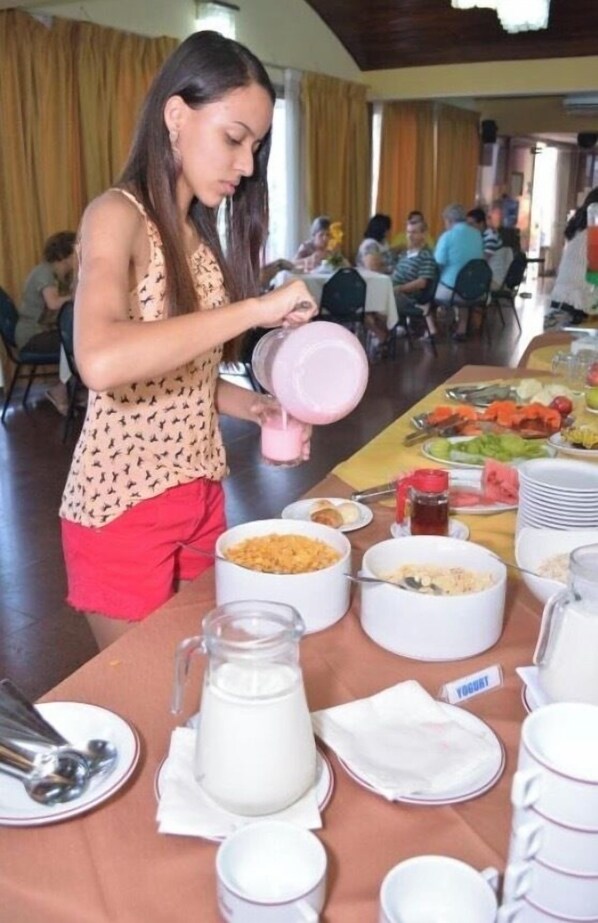 A buffet setup with various food items and a person pouring a pink liquid into a bowl. - Hotel Las Américas (Santa Cruz)