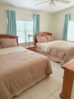 Una habitación de hotel con dos camas, un ventilador de techo y cortinas azul claro.