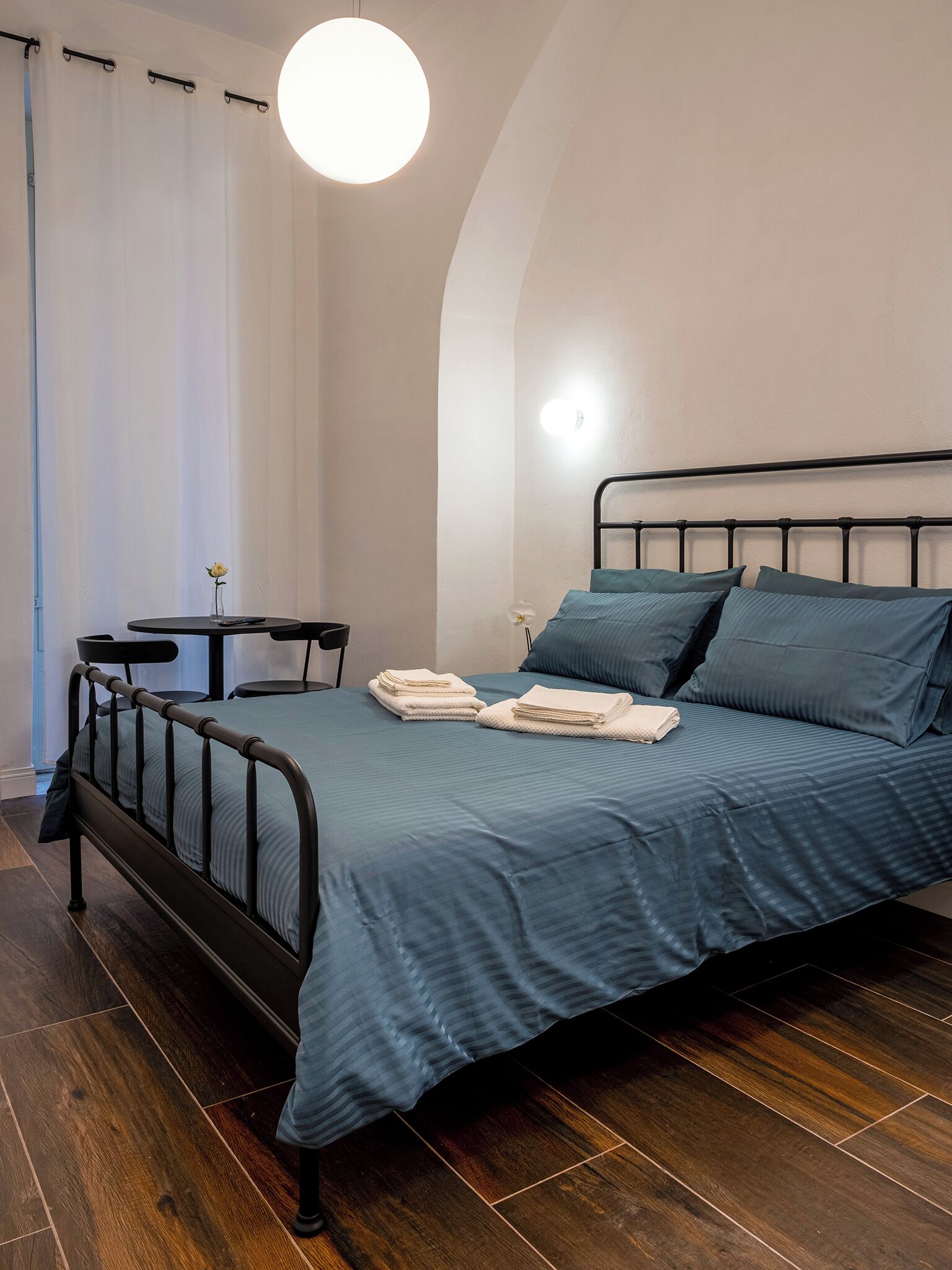 A neatly made bed with blue bedding, a small bedside table, and a lamp.