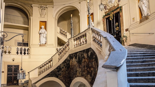 A grand staircase with ornate balustrades, a statue, and a dark marble wall. - Residenza Spinelli (Naples)