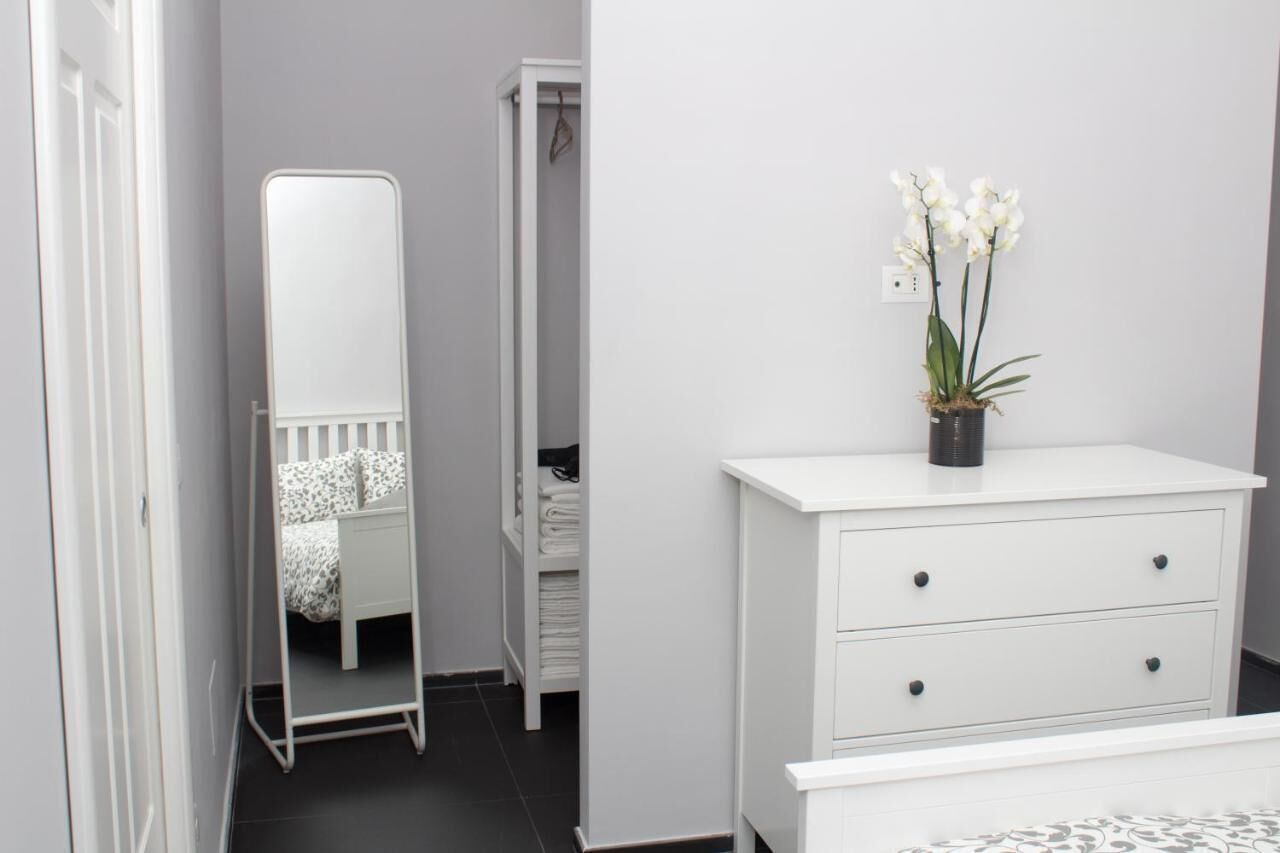 Ein Schlafzimmer mit einem weißen Bett, einer weißen Kommode, einem Spiegel und einer Topf-Orchidee.